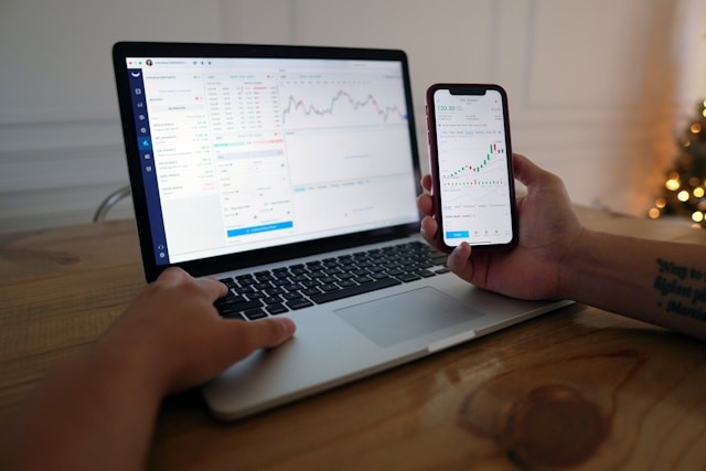 person using macbook and phone for investing